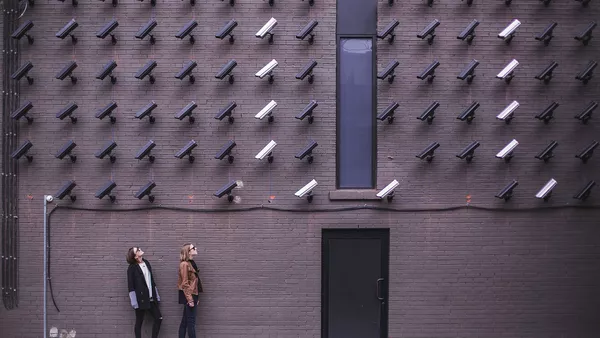 Two people look up at an abundance of CCTV cameras monitoring them.