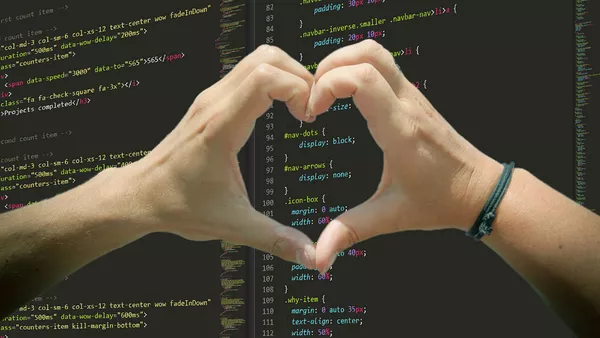 Two hands forming a heart shape with the fingers over a screen of CSS code.