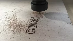 A CNC cutting machine is routing the word 'cutting' in to a sheet of wood.