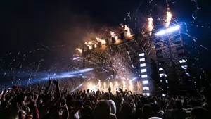 A large crowd at a concert where fireworks are exploding from around the stage.