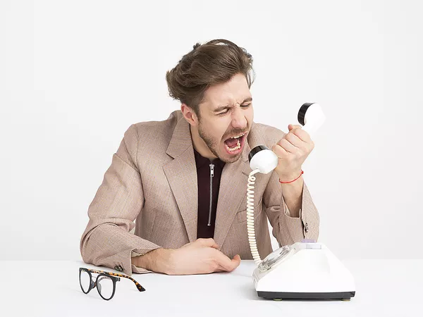 Angry man shouting through the handset of a traditional phone.