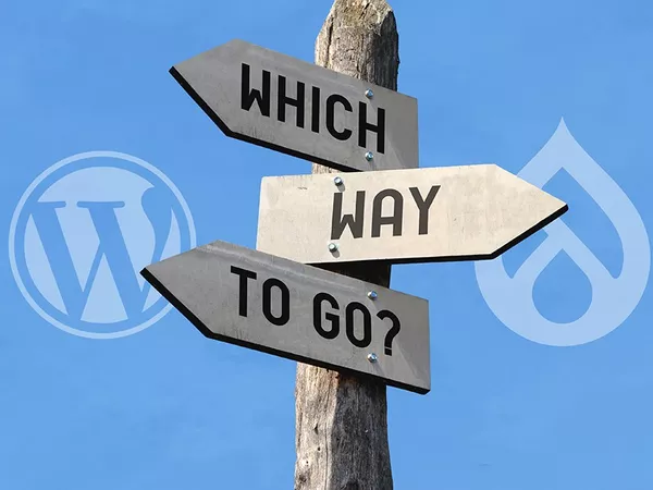 A sign post with writing Which Way To Go in opposite directions with the WordPress logo on the left and the Drupal logo on the right.