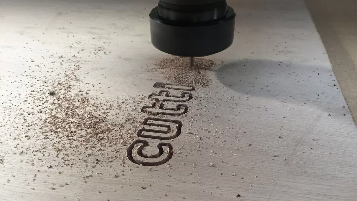 A CNC cutting machine is routing the word 'cutting' in to a sheet of wood.