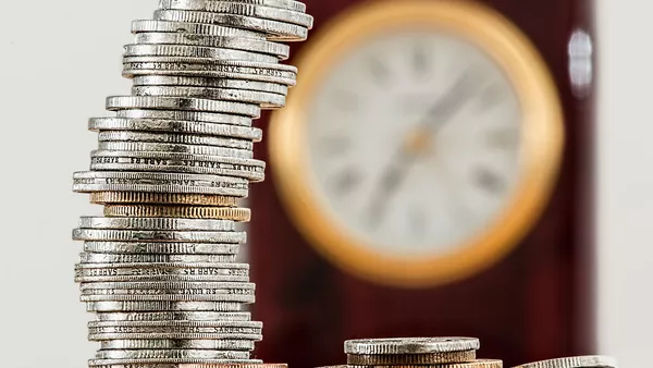 A stack of coins in front of a large (but obscured through blur) wall clock.
