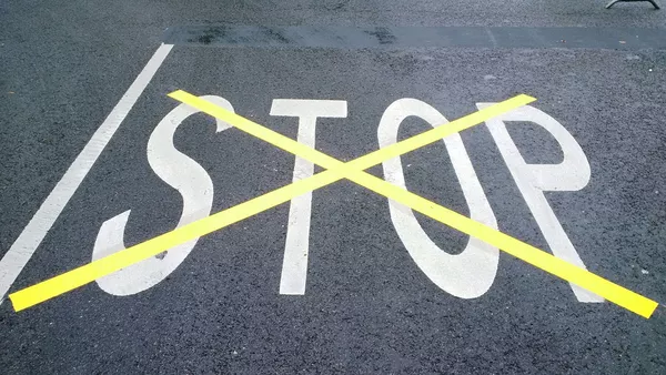 STOP painted on tarmac in white paint which has then been overpainted and crossed out with a large yellow &apos;X&apos;.