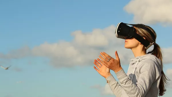 A woman wearing a virtual reality headset on a backdrop of a cloudy blue sky.