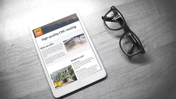 CUTcnc: Company Website Home page on an Apple iPad. Next to the device is a pair of thick rimmed glasses lying on the desk.