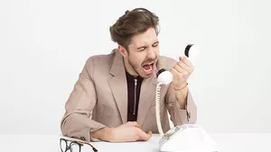 Angry man shouting through the handset of a traditional phone.