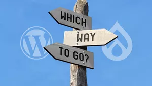 A sign post with writing Which Way To Go in opposite directions with the WordPress logo on the left and the Drupal logo on the right.